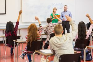 Rear view of students with hands raised in the classroom
